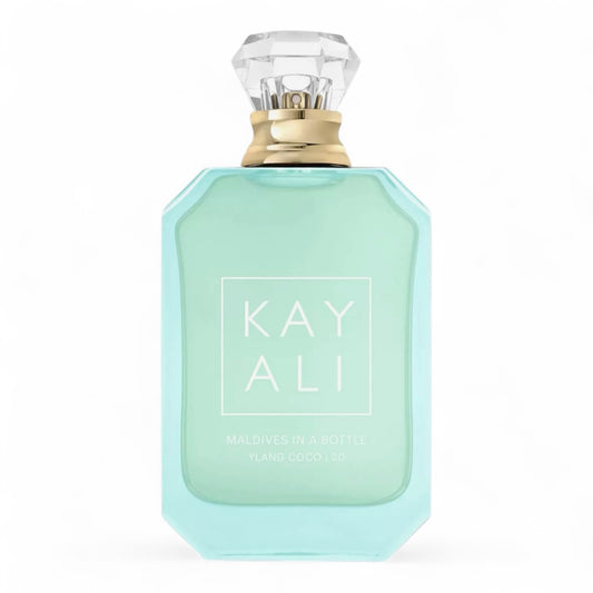 Kayali Maldives in a Bottle Ylang Coco | 20 sample surrounded by coconut halves, plumeria petals, and a tranquil ocean view.